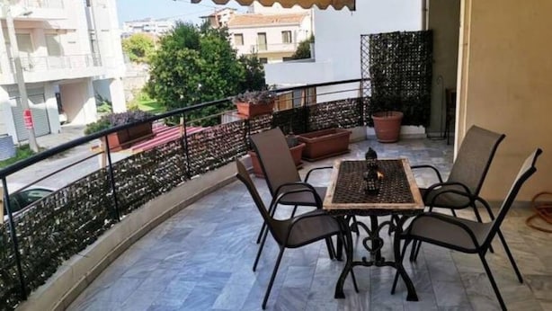 A balcony with a table and chairs, potted plants, and a view of buildings. - Alex s Apartment in Trikala (Trikala)