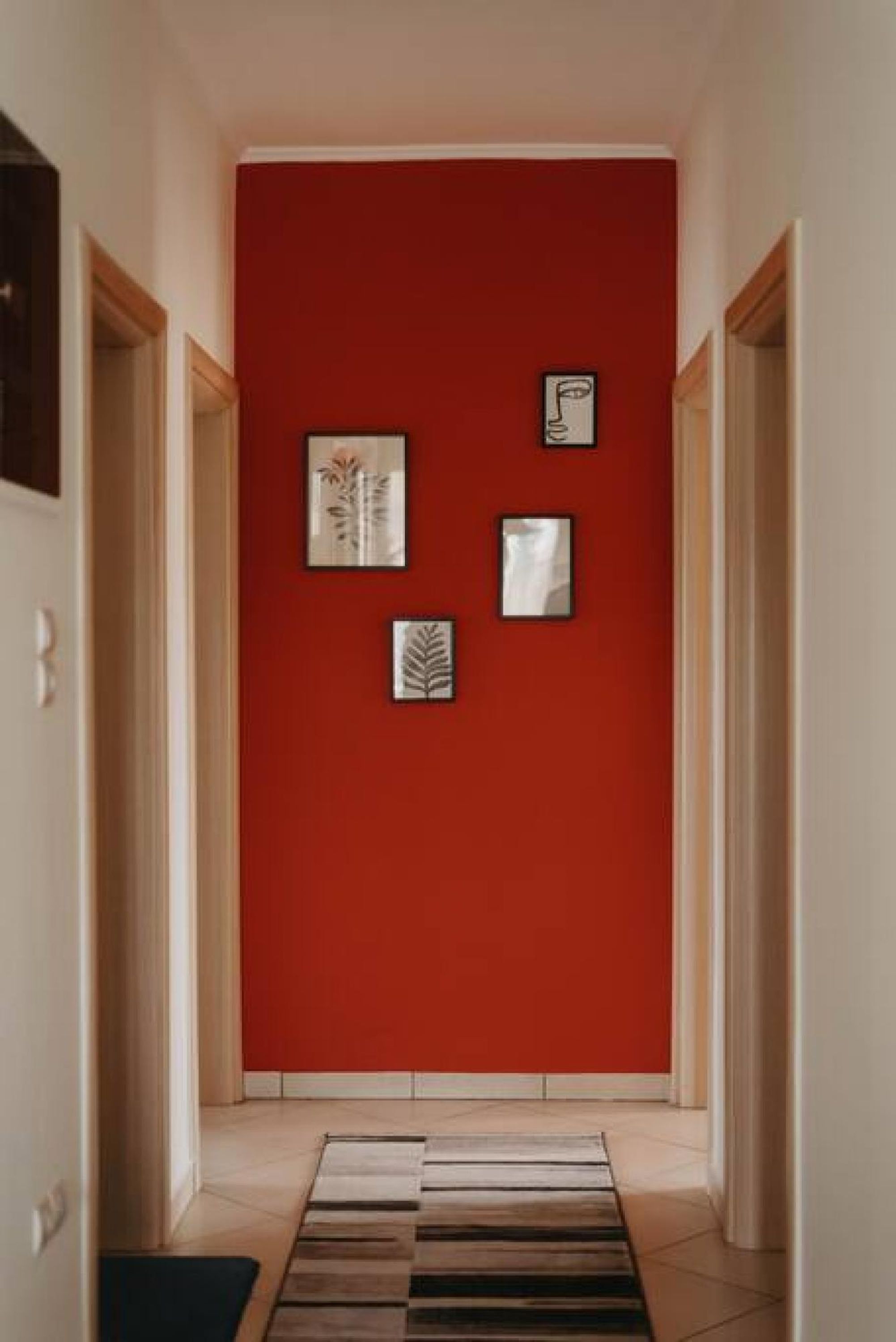 A hallway with a red wall, framed artwork, and a striped rug.