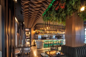 A modern bar area with a curved ceiling, green plants, and a bar counter with seating.