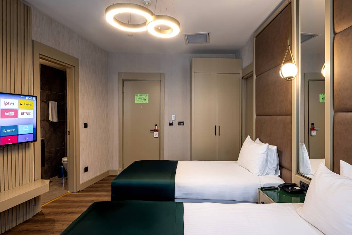 Habitación de hotel con dos camas, un televisor mostrando servicios de transmisión y un espejo que refleja la habitación.