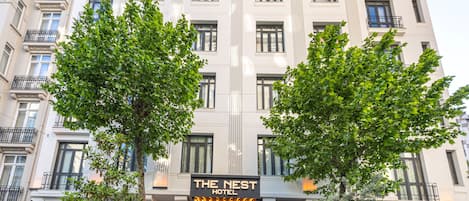 A hotel with a classic facade, a prominent entrance with illuminated signage, and a cafe to the right.