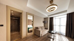 A modern hotel room with a wooden floor, a sofa, a table, a lamp, and a view of the city through large windows. - The Nest Hotel (Istanbul)