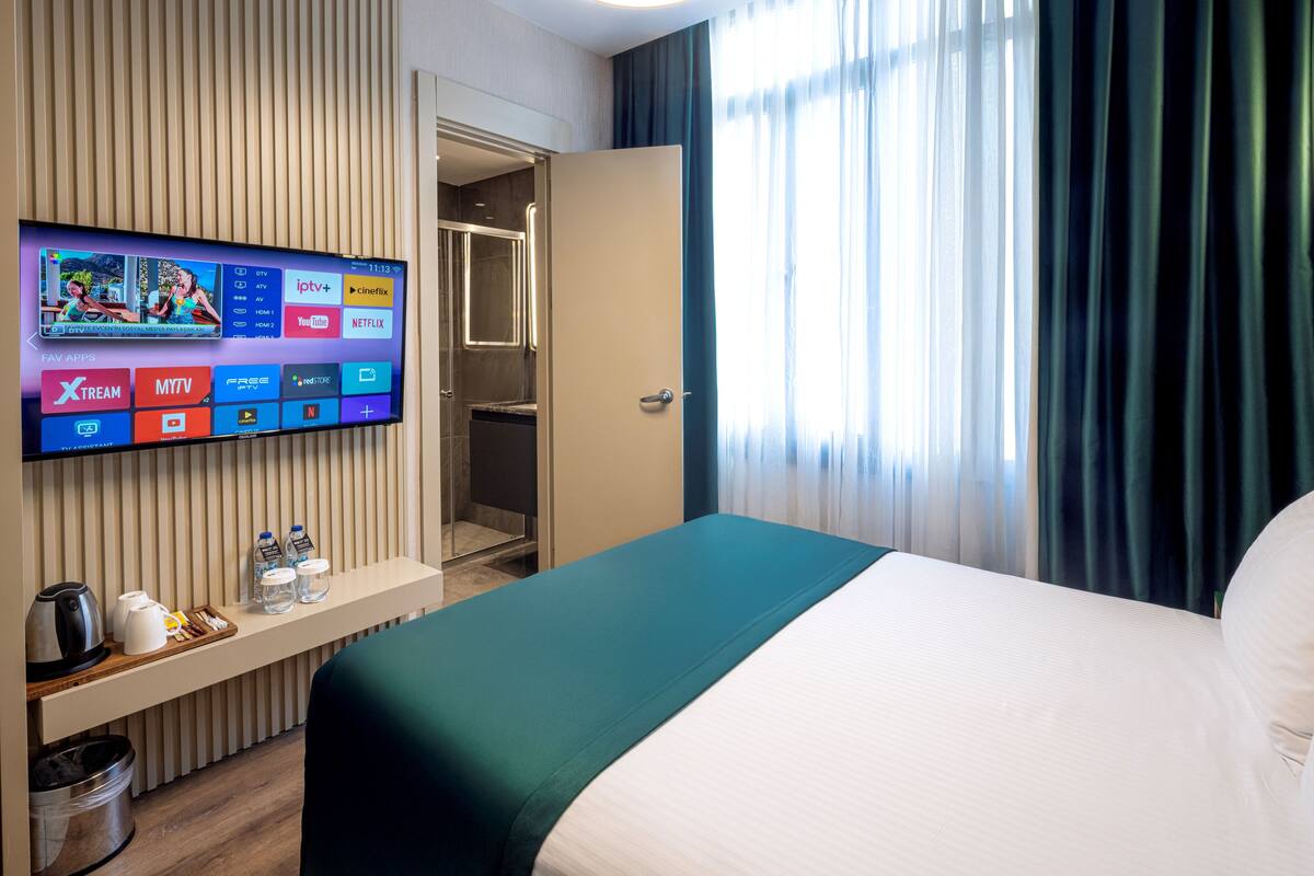 Habitación de hotel con cama, televisión mostrando servicios de transmisión, minibar y baño visible a través de una puerta abierta.