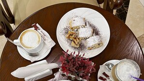 Una mesa de madera redonda con platos de pasteles, una taza de café y un vaso de una bebida cremosa.