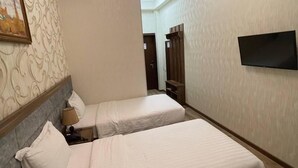 Habitación de hotel con dos camas, un televisor montado en la pared y un papel tapiz estampado.
