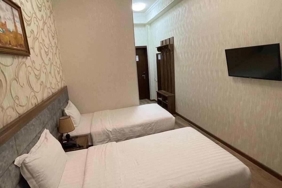 Une chambre d’hôtel avec deux lits, un téléviseur fixé au mur et un papier peint à motifs.