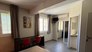 Hotellihuone, jossa on sänky, työpöytä tuolilla, televisio ja pieni keittiö.