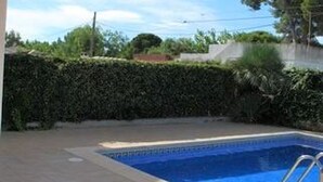 Una piscina rectangular con una escalera de metal, rodeada por un patio empinado y un seto.