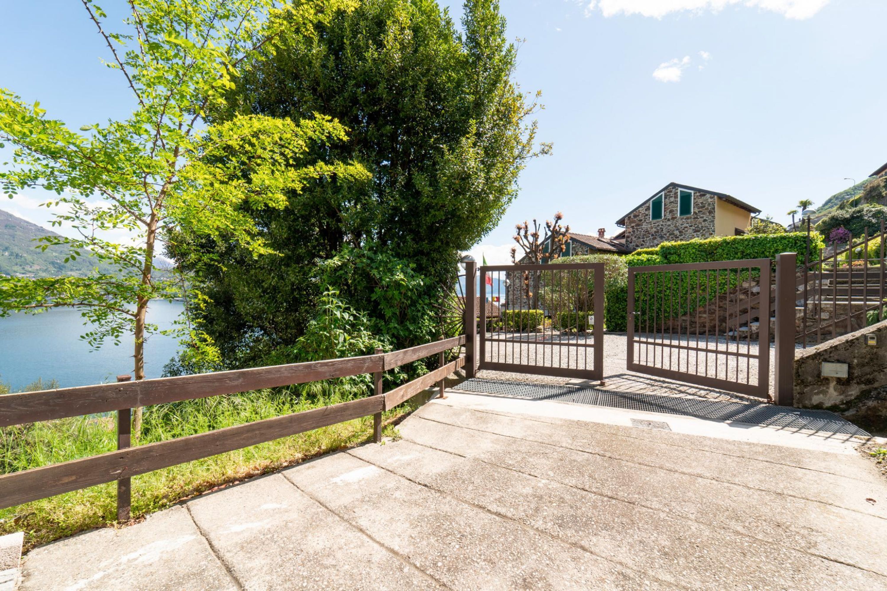 A gated entrance with a wooden fence, a stone building, and a view of a lake.