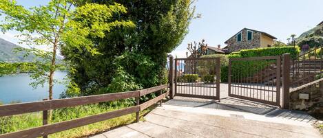 A gated entrance with a wooden fence, a stone building, and a view of a lake.