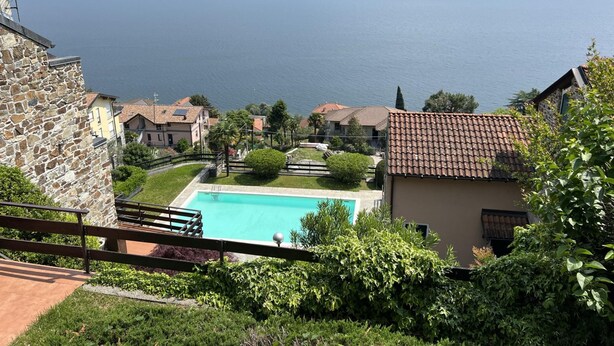 A view of a lake with a swimming pool surrounded by houses and mountains in the background. - Solelago by Wonderful Italy (San Siro)
