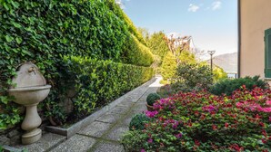 A garden pathway with a stone wall, a decorative urn, and flowering plants. - Solelago by Wonderful Italy (San Siro)