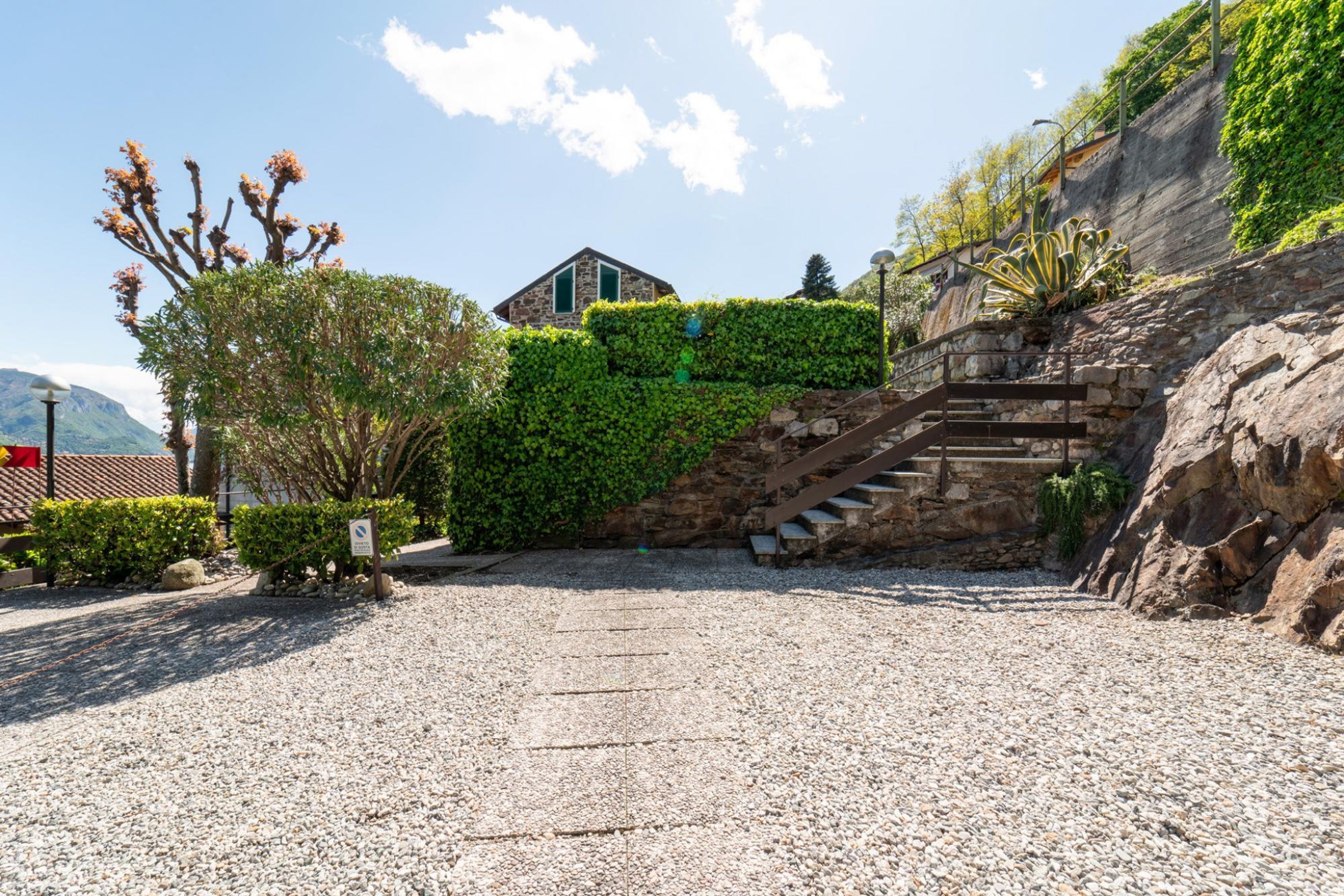 A courtyard with a gravel path, a stone staircase, and a building with a stone facade.