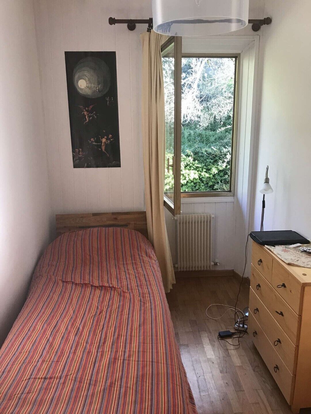 A bedroom with a bed, a dresser, a radiator, a window with curtains, and a poster on the wall.