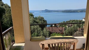 A balcony with a table and chairs, a view of a lake, and a distant mountain.