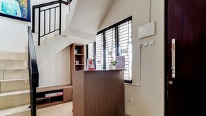A reception desk with a wooden finish, a staircase with a black railing, and a window with blinds. - OYO Life 90211 I-sidji Inn (Karawang)