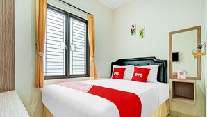 A neatly arranged hotel room with a bed, a window with curtains, a bedside table with a lamp, and a wall-mounted mirror. - OYO Life 90211 I-sidji Inn (Karawang)