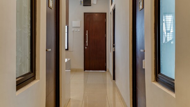 A corridor with a wooden door at the end, a wall-mounted television, and a window on the right. - OYO Life 90211 I-sidji Inn (Karawang)