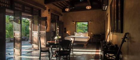 A traditional room with a bed, chairs, a table, and a view of greenery outside.