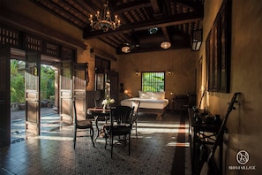 Habitación tradicional con cama, sillas, una mesa y vistas al verdor exterior.