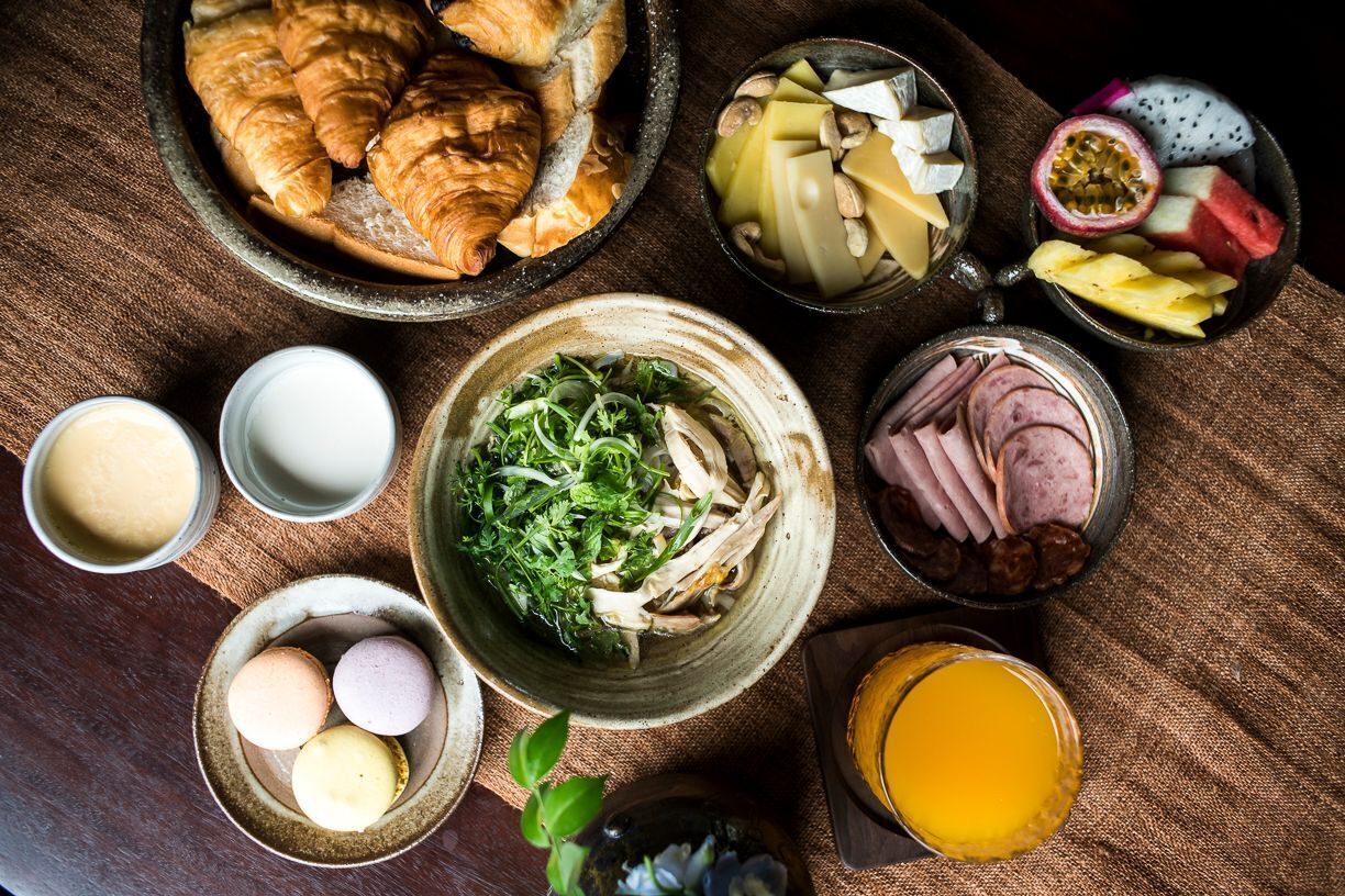 A table with various food items including croissants, cheese, fruits, and a bowl of greens.