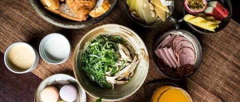 A table with various food items including croissants, cheese, fruits, and a bowl of greens.