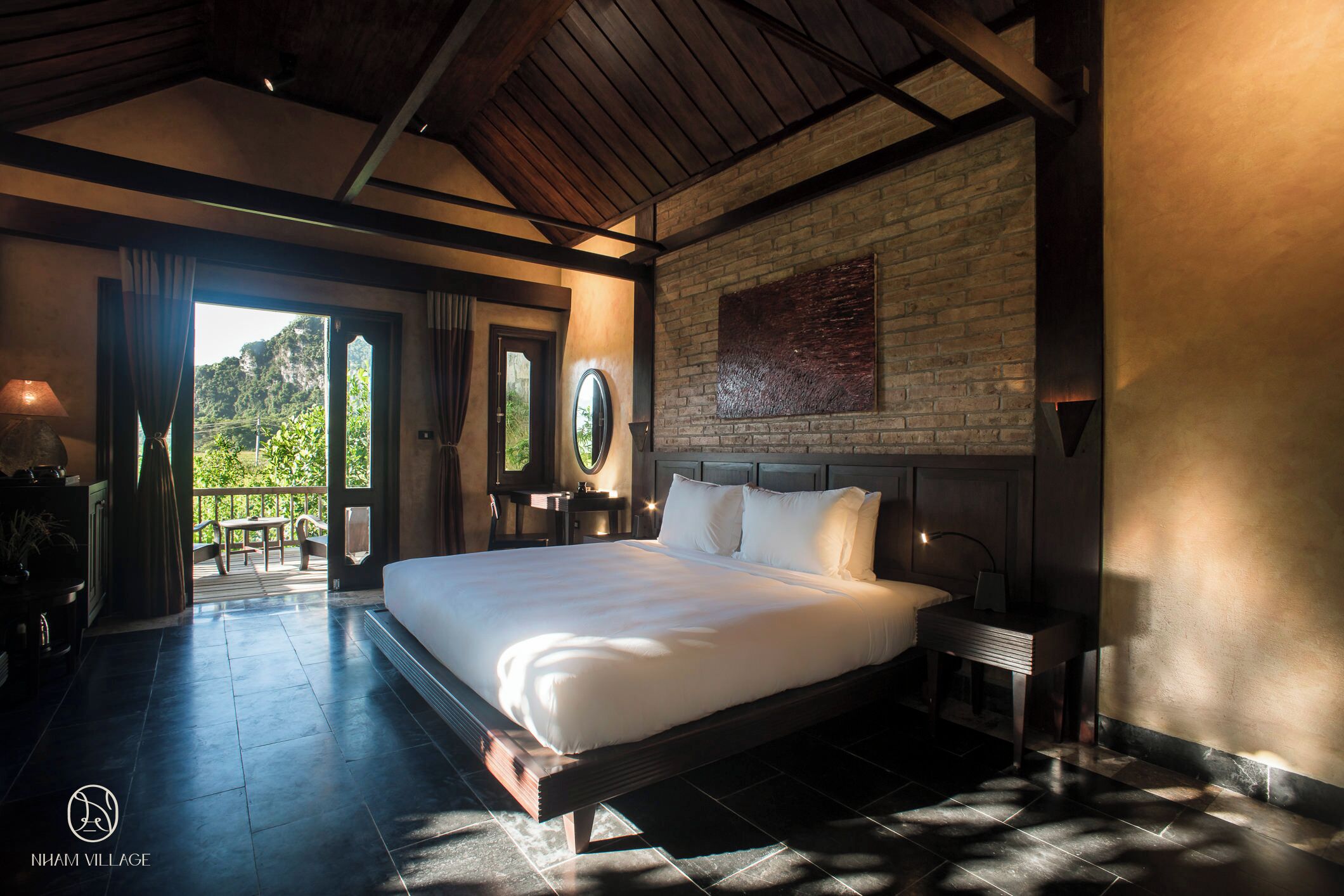 A large bed in a well-lit bedroom with a view of greenery outside.