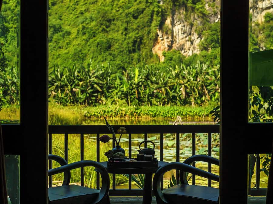 A wooden deck with two chairs and a table, overlooking a lush green landscape with a water body and a mountain.