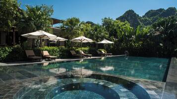 A swimming pool with lounge chairs and umbrellas, surrounded by lush greenery and mountains.