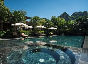 A swimming pool with lounge chairs and umbrellas, surrounded by lush greenery and mountains. - Nham Village Resort (Nam Hoa Lu)