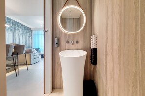 A modern bathroom with a large white sink, a round mirror with a light, and a towel rack.