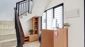 A staircase with a wooden handrail and a black metal railing, leading to a wooden reception desk with a red logo. - Hotel O Marta Residence (Karawang)