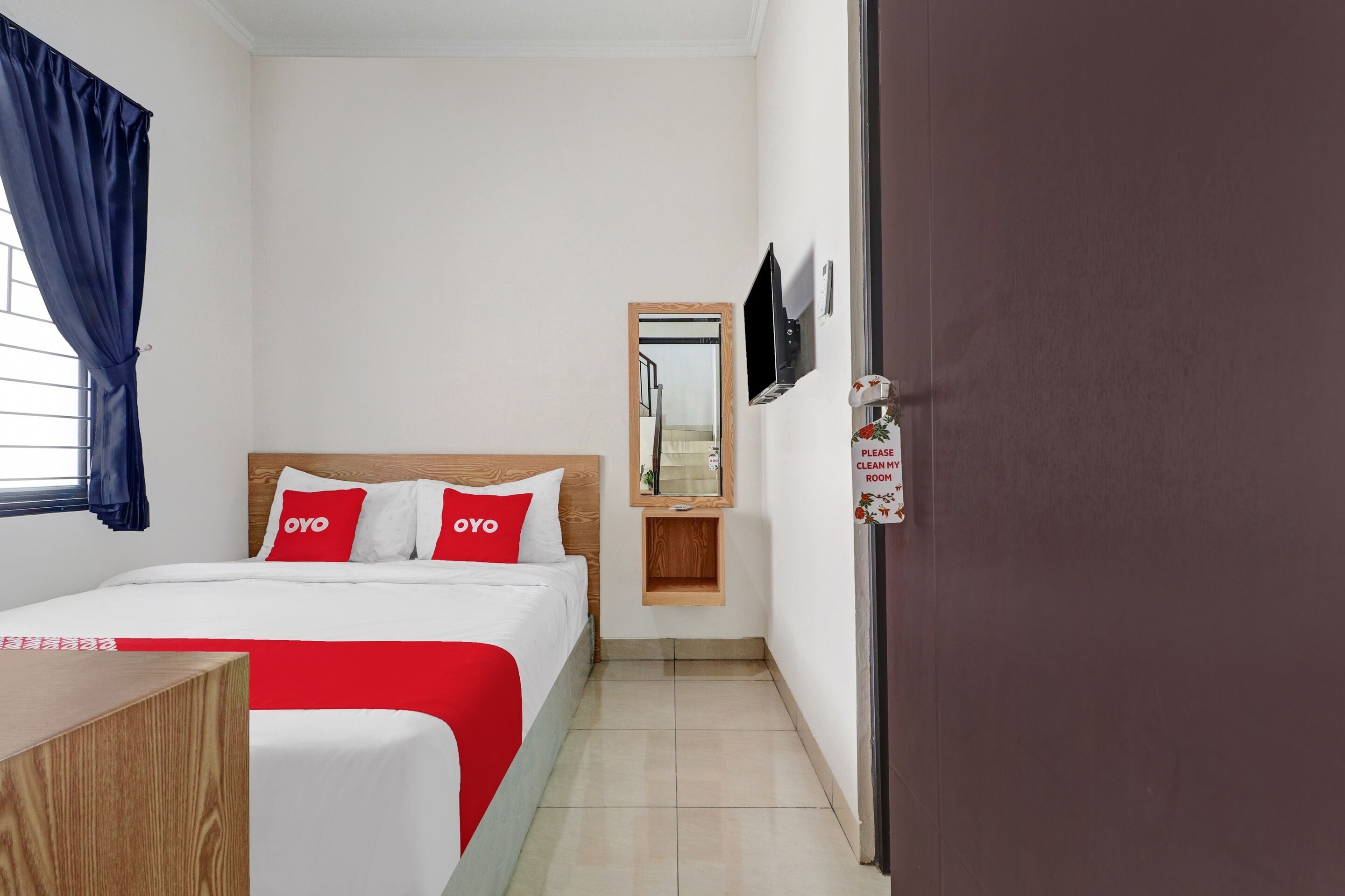 A hotel room with a bed, a desk, a mirror, and a door with a sign.