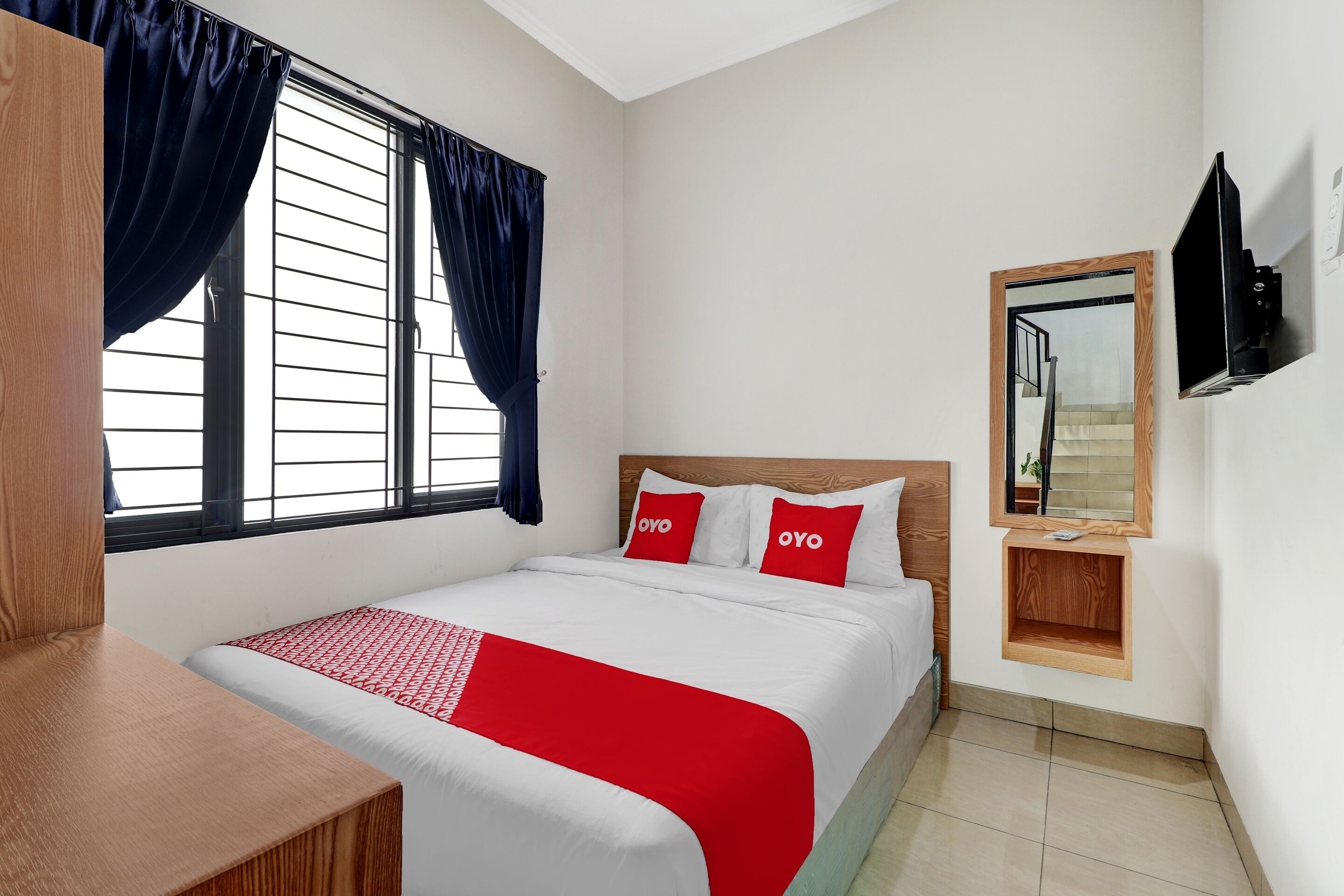 Habitació d'hotel amb un llit, escriptori de fusta, televisió penjada a la paret i finestra amb cortines.