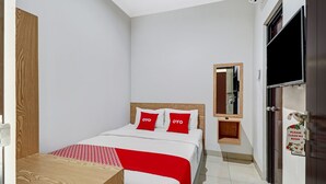 A clean, modern hotel room with a neatly made bed, a wooden nightstand, a small wooden cabinet, a mirror, and a TV mounted on the wall. - Hotel O Marta Residence (Karawang)
