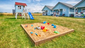 A sandy play area with toys, a slide, and a small building with a red roof. - Cozy home in Jaroslawiec (Jaroslawiec)