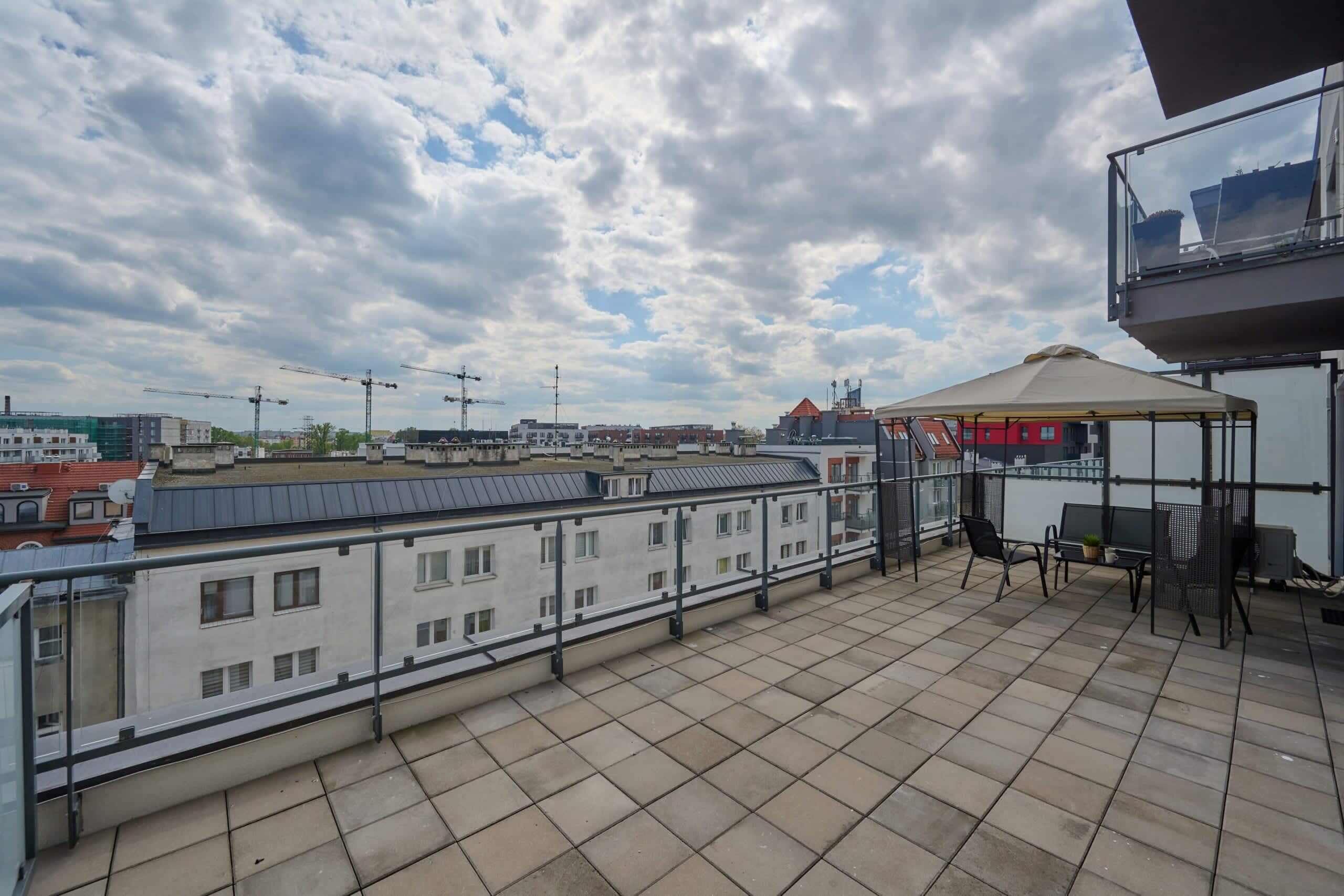 Une terrasse sur le toit offrant une vue sur les bâtiments environnants, un espace salon couvert et une rambarde.