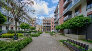 Un sendero conduce a un edificio de varios pisos, rodeado de follaje y bancos.
