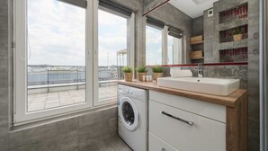 Un apartamento moderno con un ventanal grande, lavadora, lavabo y estanterías empotradas con cestas.