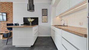 Una cocina moderna con una isla central, armarios blancos, una pared de ladrillo decorativa y un televisor montado.
