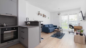 A modern kitchen with grey cabinets, a built-in oven, and a dining area with a blue sofa and a small table.