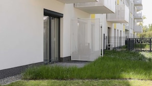 A modern building with balconies, a glass door, and a grassy area.