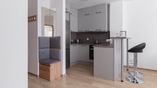 A modern kitchen with grey cabinets, a wooden stool, a bar stool, and a small island with a sink.