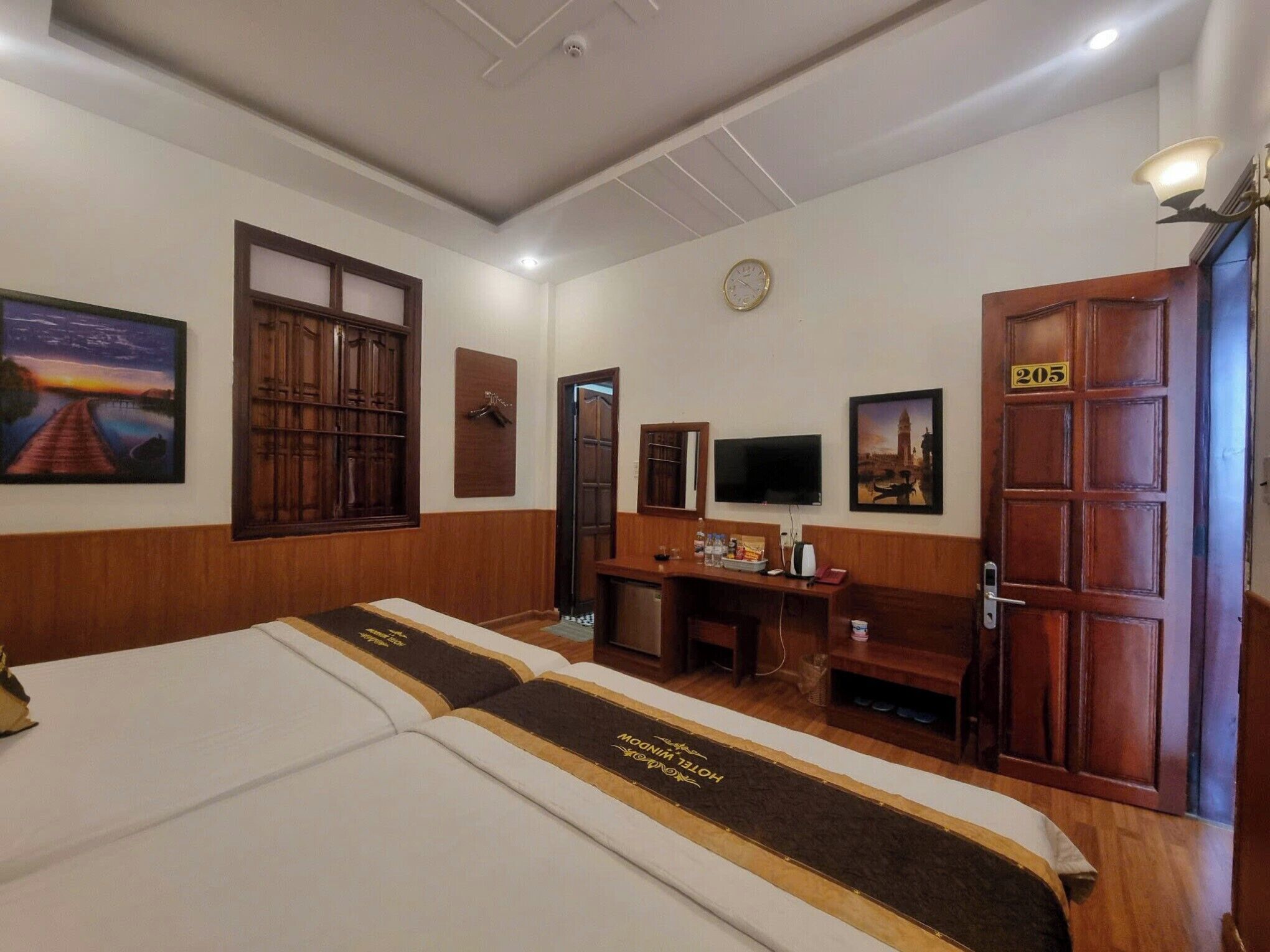 Une chambre d’hôtel équipée d’un lit, d’un bureau, d’une télévision et d’une porte portant le numéro 205.