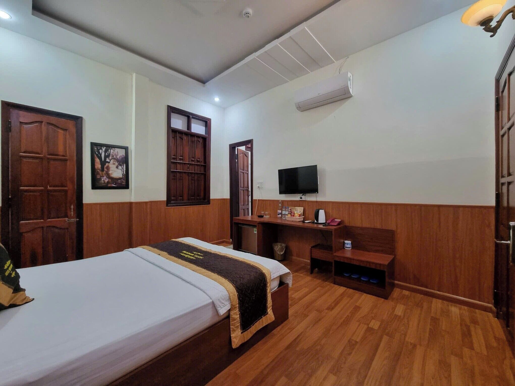Quarto com cama, guarda-roupa de madeira, escrivaninha, televisão e ar condicionado.