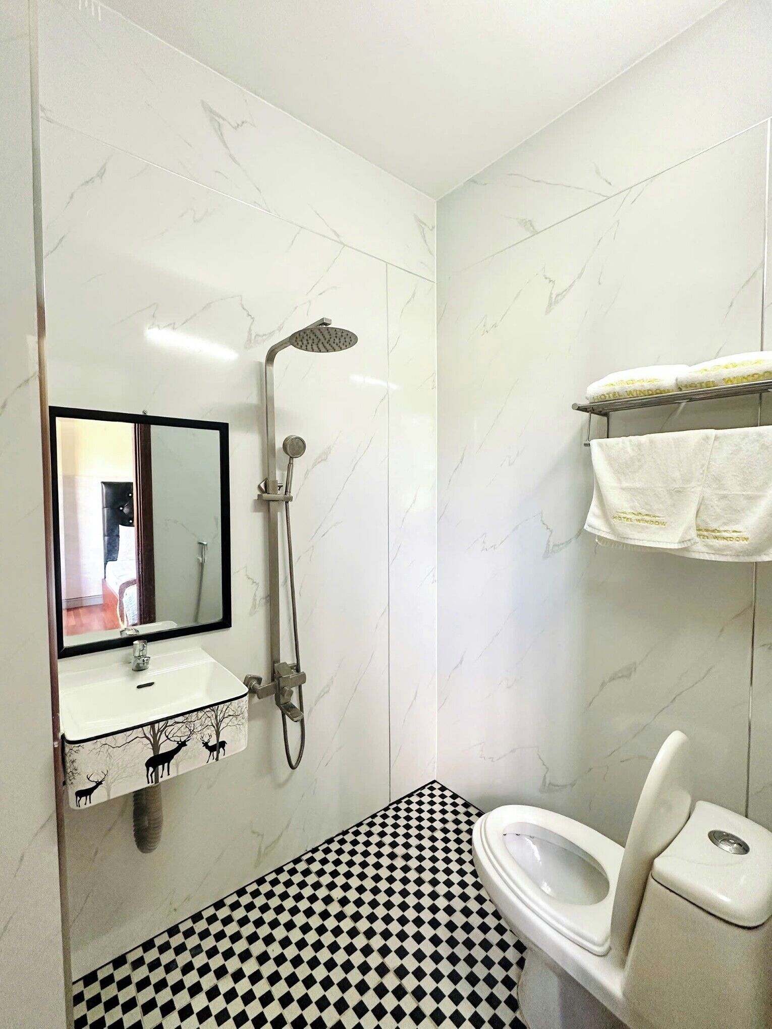 A bathroom with a white sink, a mirror, a shower, a toilet, and a checkered floor.