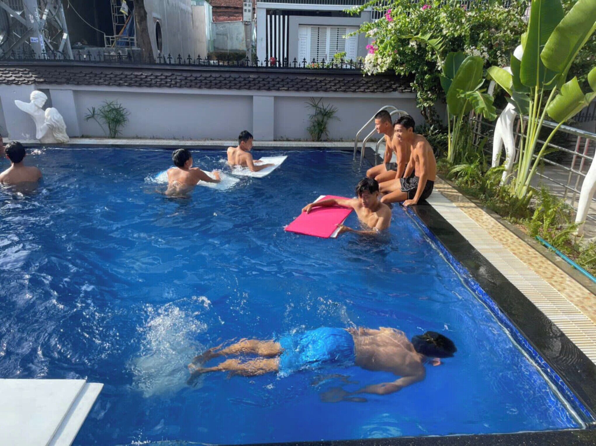 Una piscina con persone che nuotano, una postazione di salvataggio e un tappetino rosso.