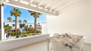 Un balcon avec une table et des chaises, donnant sur une cour intérieure agrémentée de palmiers et de bâtiments.