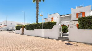 Un chemin piétonnier dallé mène à un bâtiment blanc doté d’un balcon et de volets orange.