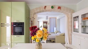 Une cuisine équipée d’un four encastré, une table à manger agrémentée d’un vase de fleurs et un coin salon avec un lit et une fenêtre.